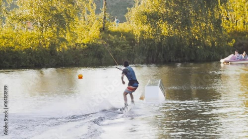 Wakeboarder ride on cable wakeboard in park, outdoor extreme slow motion on water, surfing athlete on water doing boardslide, noseslide or tailslide 180 out photo