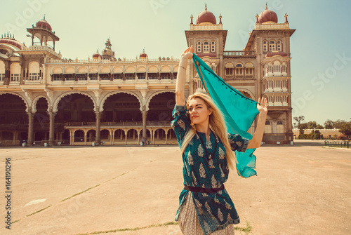 Beautiful happy woman with headscarf dancing around building with towers of the royal Palace of Mysore, Karnataka state, India.