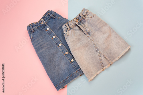 Fashionable concept. Two denim skirts, blue and gray. Tender pink and blue background.