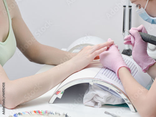 Girl in gloves handles nails with a milling cutter for manicure