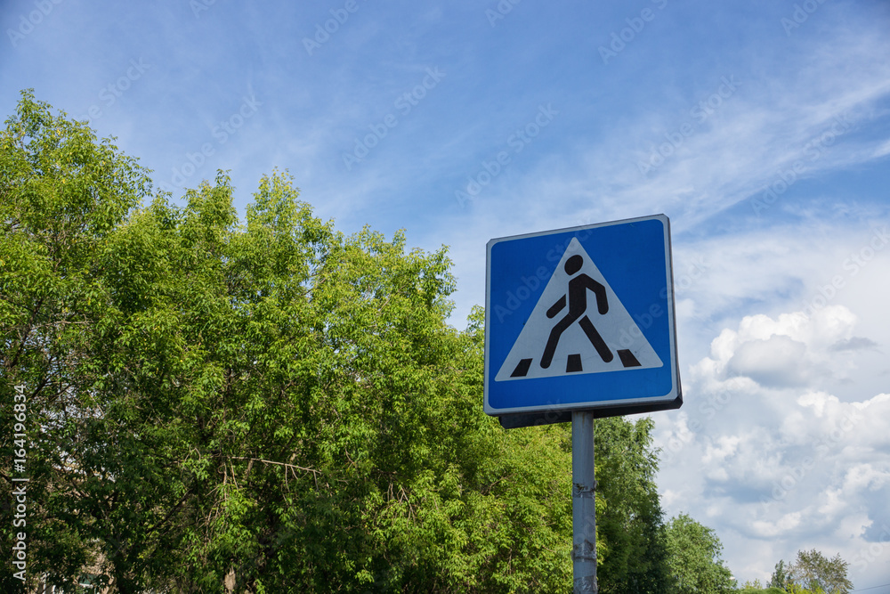 Pedestrian crossing sign with a blue sky and green trees on background