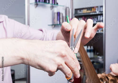 A hands of hairdresser making a haircut for a blonde girl