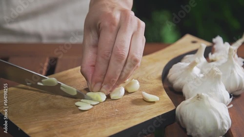 Chef shreds garlic on the wooden board near the grill's fire, makinf the salad, vegetable meal, vitamins in daily food, cooking outdoors photo