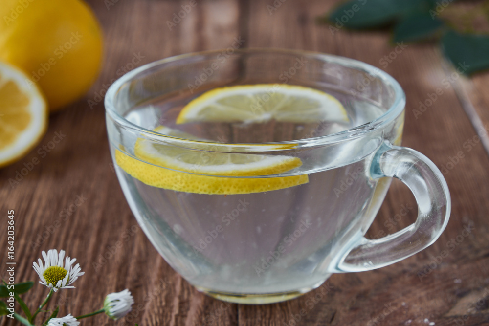 Delicious tea with lemon on a wooden background. A slice of lemon on the table. Water with lemon. Delicious tea with lemon on a wooden background. A slice of lemon on the table. Water with lemon.
