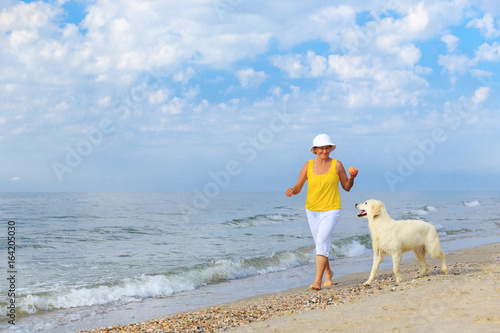 Happy elderly woman walking along a beach with her golden retriever at the morning