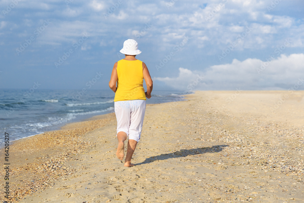 senior woman jogging on sea beach at the morning, back view