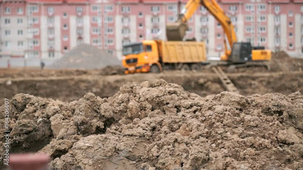 Yellow excavator loads clay using its big bucket in the background residential development. Construction area in summer Yellow excavator loads clay using its big bucket in the background residential development. Construction area in summer