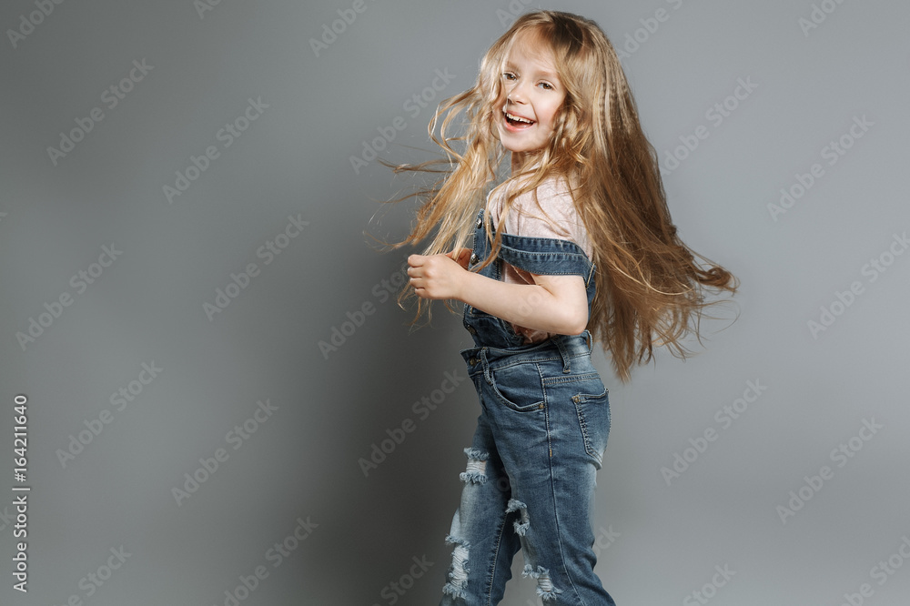 Happy and funny stylish little girl smiling in fashion jeans over grey background. Happy and funny stylish little girl smiling in fashion jeans over grey background.