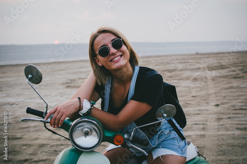 Young female laughing while sitting on retro scooter on the beach