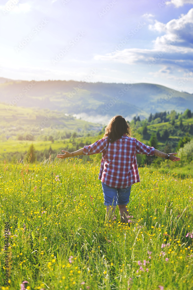 The girl raised her hands and stands on a meadow in the mountains in the summer The girl raised her hands and stands on a meadow in the mountains in the summer