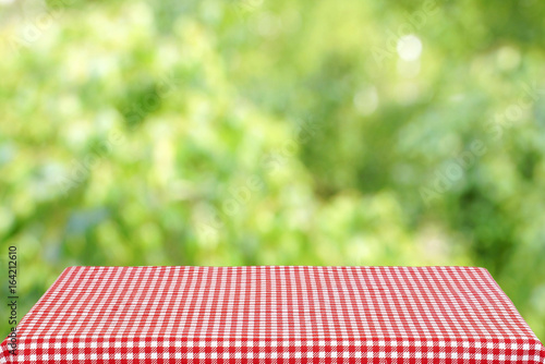 Empty table with a red checkered cloth in the summer garden. Blurred background.