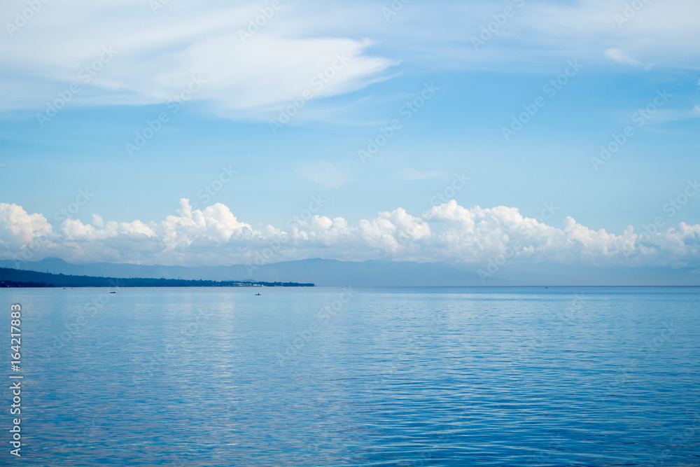 Tropical seascape with distant island and blue sky. Relaxing sea view with still seawater.