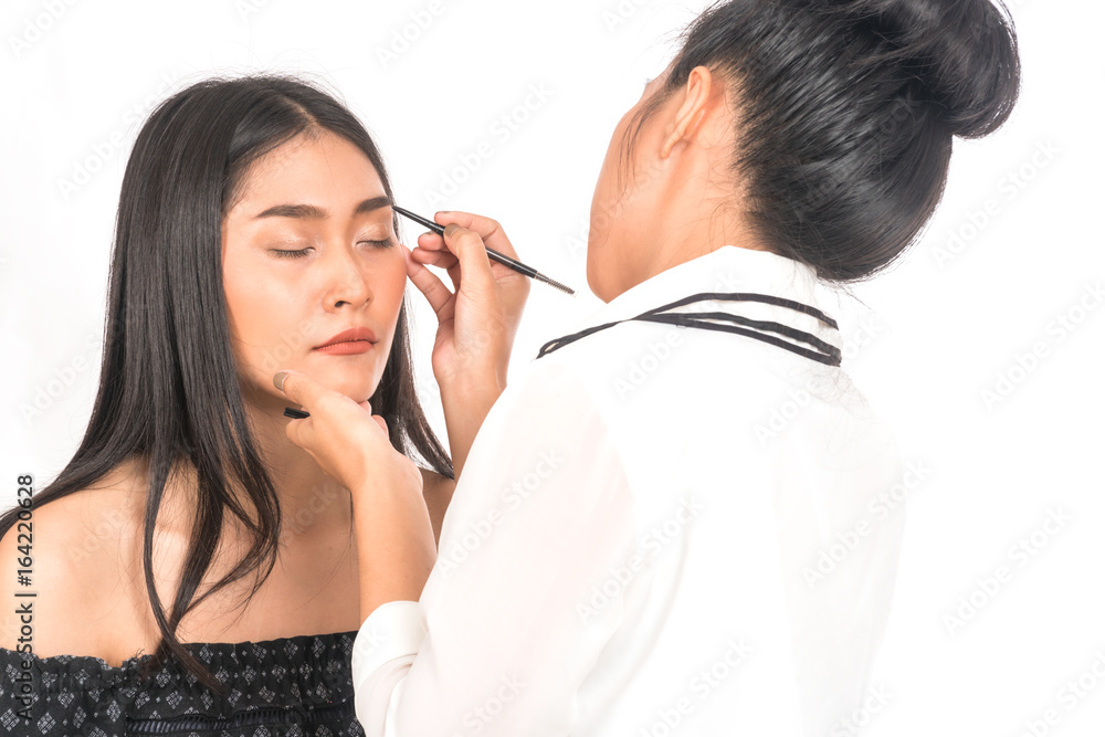 Asian Makeup artist applying Eyeliner for beautiful young woman on white background. Asian Makeup artist applying Eyeliner for beautiful young woman on white background.