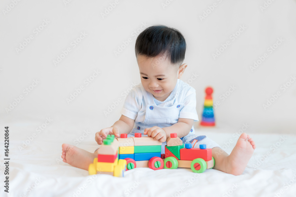 Adorable Asian baby boy 9 months sitting on bed and playing with color wooden train toys at home.. Adorable Asian baby boy 9 months sitting on bed and playing with color wooden train toys at home..