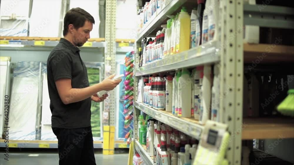 Man in the mall in department of household chemicals. He choosing cleaner sprayer and taking one of them from the shelf. Man in the mall in department of household chemicals. He choosing cleaner sprayer and taking one of them from the shelf.