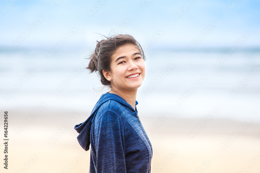 Happy, smiling teen girl in blue hoodie jacket on beach Happy, smiling teen girl in blue hoodie jacket on beach