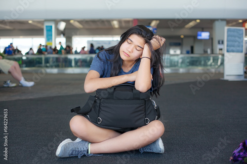 Tired teen girl sitting on floor at airport with luggage