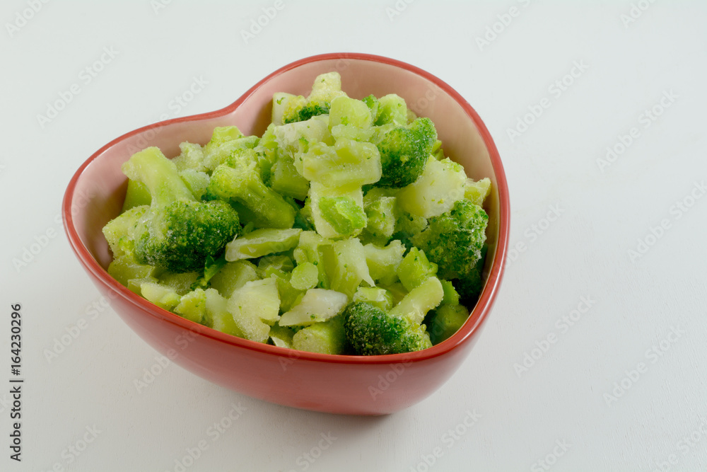 Heart healthy frozen broccoli cuts in heart shaped bowl on white wooden table Heart healthy frozen broccoli cuts in heart shaped bowl on white wooden table