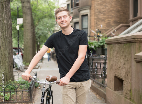 Portrait of young modern hipster man pushing bicycle on a residential street in the city