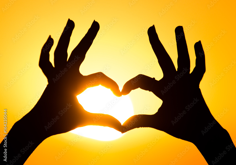 Silhouette of the heart by hands at sunset