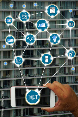 Internet of things (IOT) concept : Hand holding smartphone controlling various household equipment with building background. Smart home concept, Smart Building Concept.