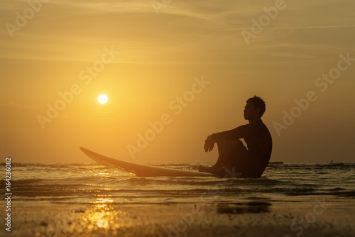 Man sitting with surfboard on the beach.