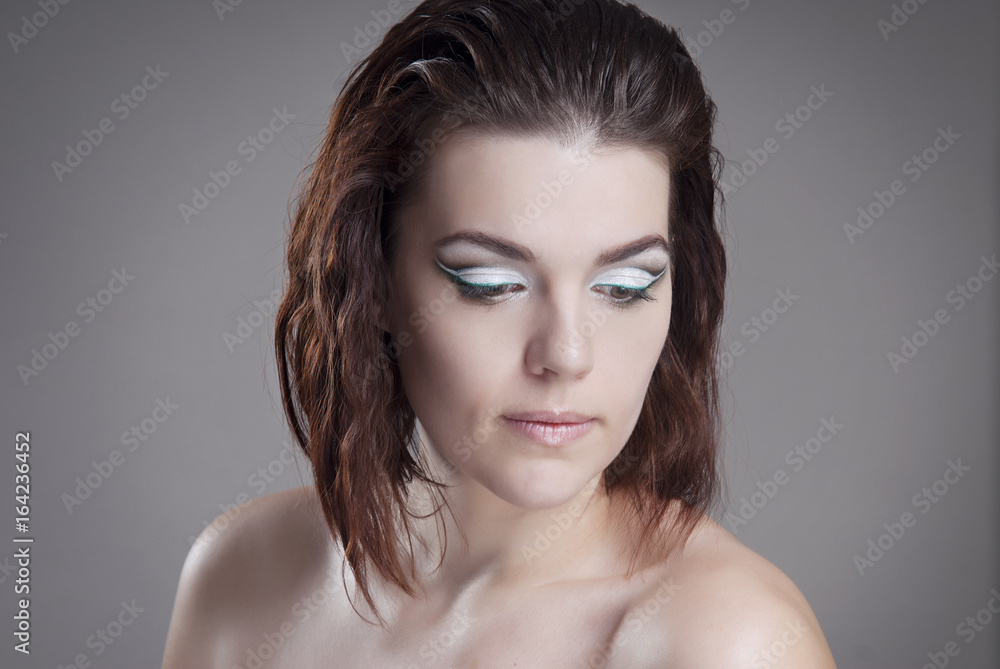 The girl the brown-haired woman with bright makeup looking down. Isolated grey background. Hairstyle graduated bob. The girl the brown-haired woman with bright makeup looking down. Isolated grey background. Hairstyle graduated bob.