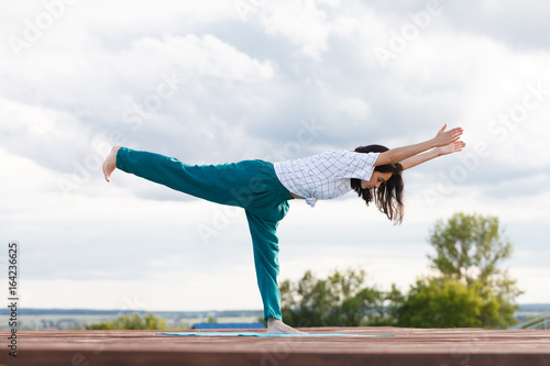 Young girl doing yoga or fitness exercise outdoor in nature with beautiful sky landscape, Namaste pose. Meditation and Relax, freedom concept