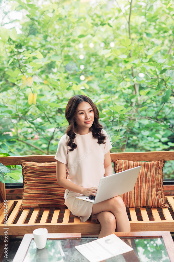 Beautiful young smiling woman working on laptop while sitting on bed at home near big window. Beautiful young smiling woman working on laptop while sitting on bed at home near big window.