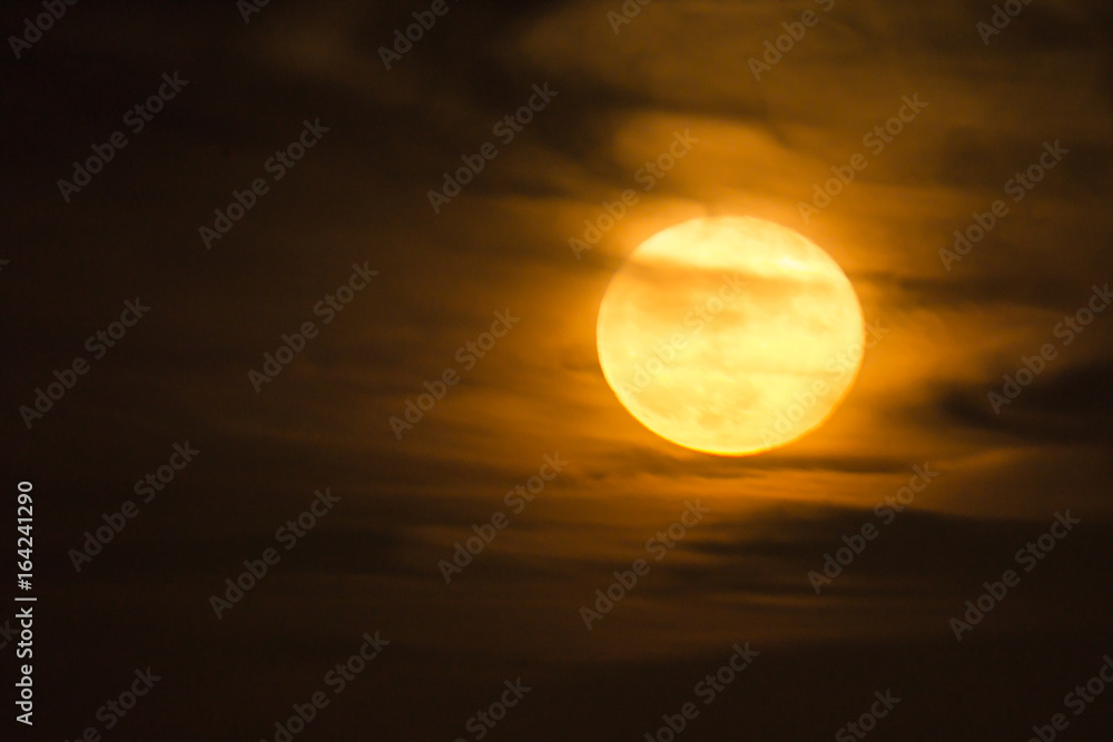 a warm orange full moon rises into a cloudy night sky