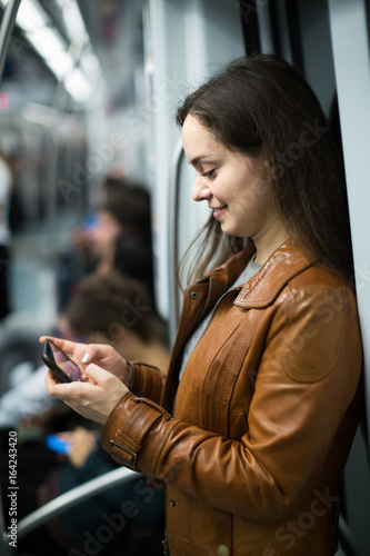 brunette girl using cell phone and smiling at subway