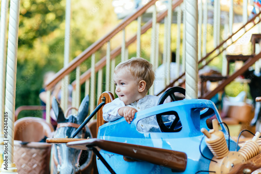 Happy little boy with blonde hair and blue eyes sitting in vintage blue airplane on carousel Happy little boy with blonde hair and blue eyes sitting in vintage blue airplane on carousel