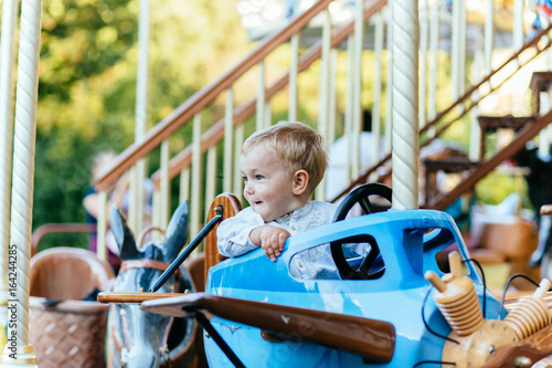 Happy little boy with blonde hair and blue eyes sitting in vintage blue airplane on carousel