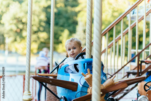 Happy little boy sitting in a vintage blue airplane on the merry-go-round