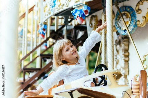 Happy 5-year-old girl riding on a merry-go-round and holding hands like an airplane