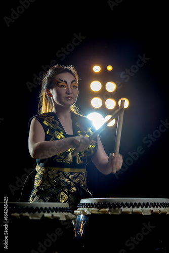 beautiful asian drummer girl with drumsticks, studio shot on a dark background.
