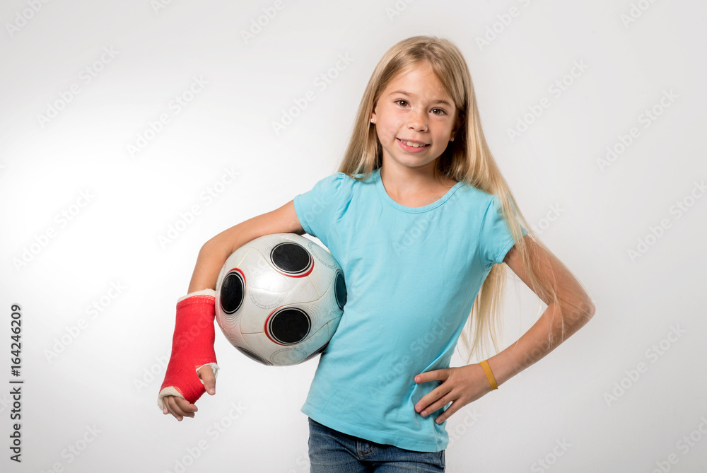 junges Mädchen mit gebrochenem Arm hält Fußball und lächelt in die