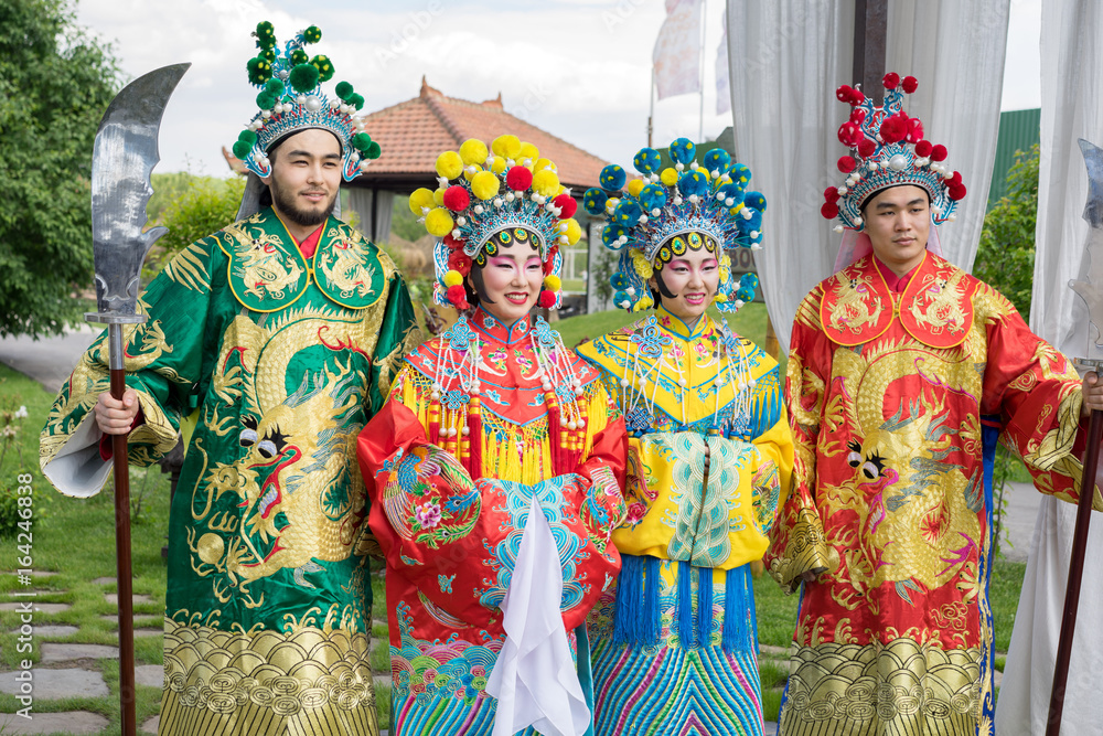 group of four asian people men and women standing in a row and greeting outdoor in traditional chinese costumes