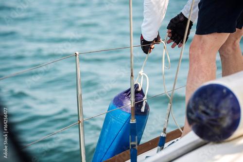 Sailor tied fenders on a yacht during the mooring to the shore.