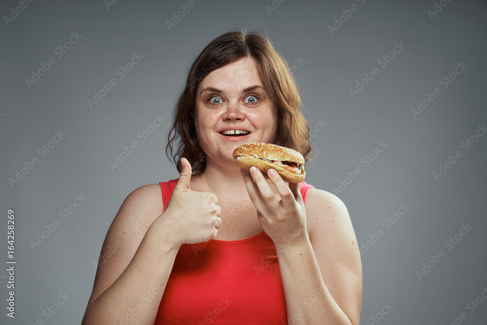 Fat woman on a gray background holds a hamburger Fat woman on a gray background holds a hamburger