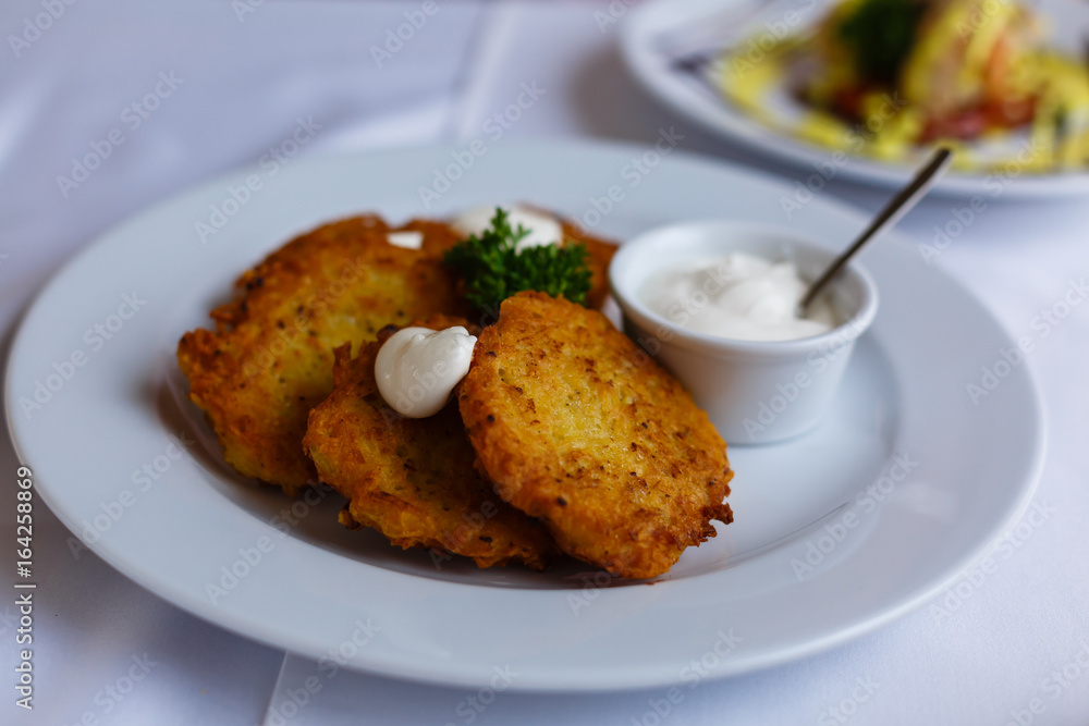 Potato pancakes - draniki - with sour cream in a white plate. The national dish of Russian, Ukrainian and Belarusian cuisine Potato pancakes - draniki - with sour cream in a white plate. The national dish of Russian, Ukrainian and Belarusian cuisine