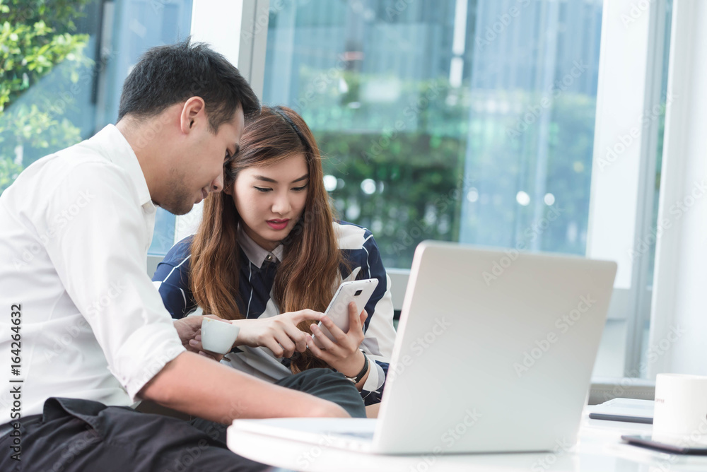 Two asian coworkers use laptop and smartphone work together having coffee Two asian coworkers use laptop and smartphone work together having coffee