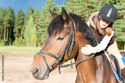Girl equestrian riding horseback and stroking horse neck. Summertime outdoors