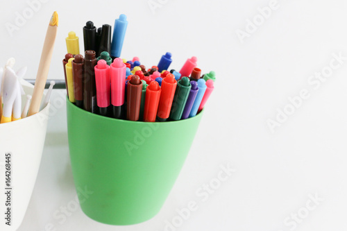 colorful markers in green cup is hanged on the bar with white wall