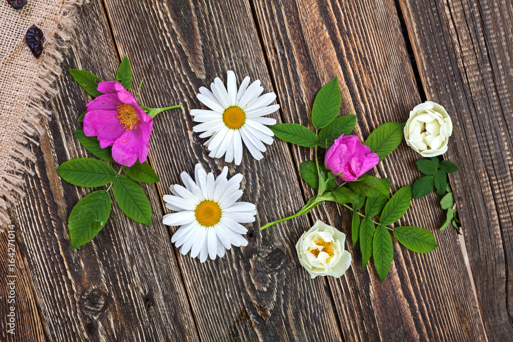 Obraz premium Flowers of chamomile and rose hips on a rough wooden village table
