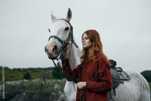 Beautiful young woman in the mountains walking with her horse