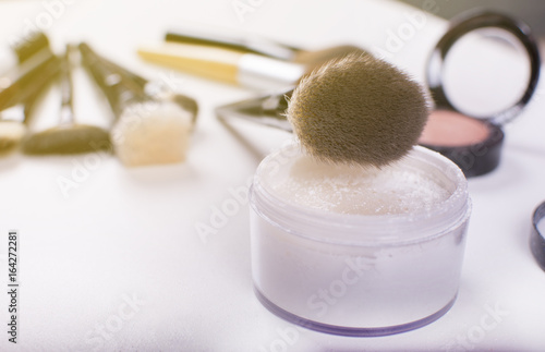 Close up look at the soft cosmetics brush and face powder over a white background. Beauty and makeup concept. Colorful frame with various makeup products on a white background.