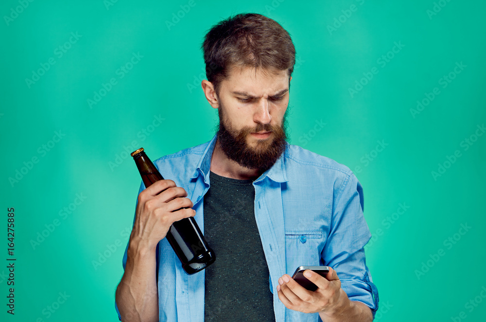 A young guy with a beard on a green background holds a bottle of beer A young guy with a beard on a green background holds a bottle of beer