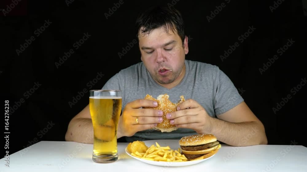 Overweight young man drinking beer and eating a burger