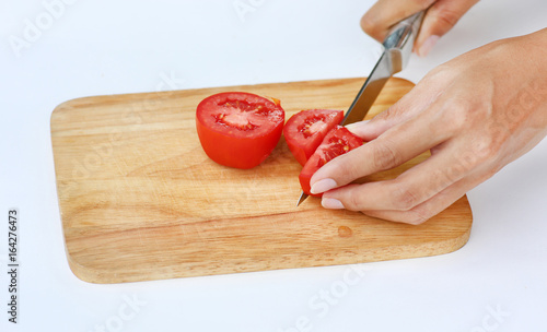 Tomato slices on wood block with knife against white background.